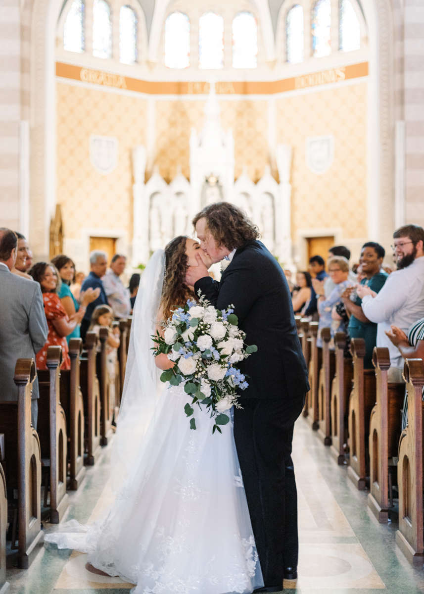 Newlywed couple sharing a romantic kiss at the end of the aisle inside the breathtaking Immaculate Conception Cathedral in Lake Charles, Louisiana